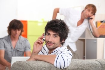 Handsome young man making a call with his friends doing the same in the background