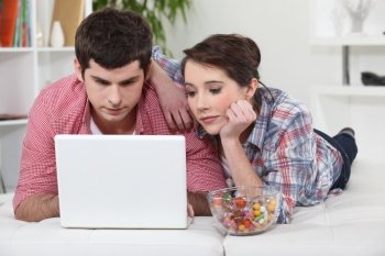 Couple laying in bed with laptop and sweets