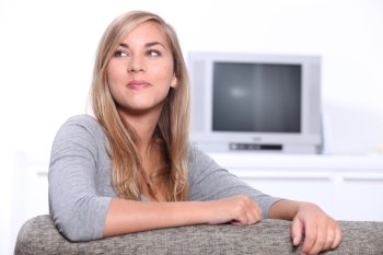 Smiling young woman sitting on a couch with a television set in the background