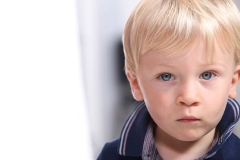 Landscape portrait of a serious little boy with blonde hair and blue eyes