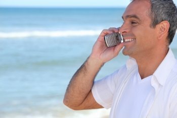 Smiling man using a cellphone by the ocean