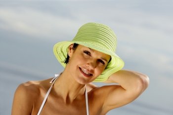 Brunette holding on to her hat at the beach