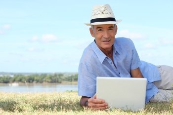 Senior man using a laptop computer on a riverbank