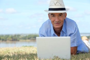 Senior man lying on the grass with a computer