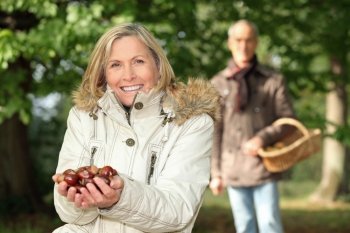 mature woman in woods with husband showing chestnuts