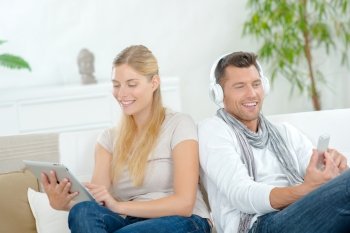 Couple sat on sofa, each using technology