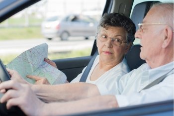 Elderly couple driving, wife pointing to map