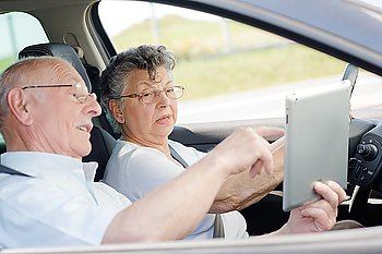 Elderly couple in car, woman driving, man showing screen of tablet