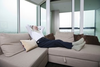 Full length of senior man relaxing on sofa with hands behind head at home