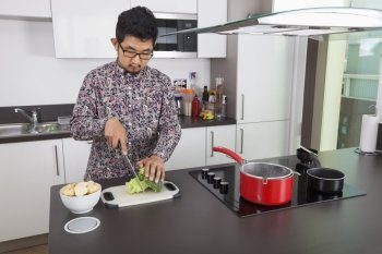 Young man chopping broccoli at kitchen counter