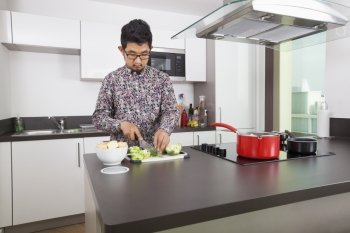 Young man cutting broccoli at kitchen counter