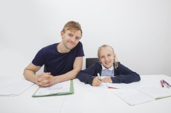 Portrait of mid adult man sitting with daughter studying at table