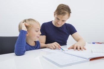 Mid adult man assisting boy in studies at table