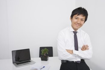Portrait of happy mid adult businessman with arms crossed leaning on office desk