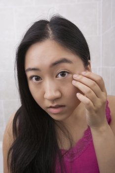 Portrait of beautiful young woman inspecting her face in bathroom