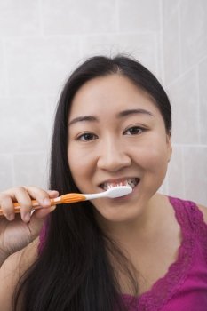 Close-up view of young Asian woman brushing her teeth in bathroom
