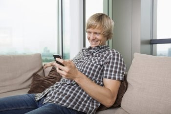 Smiling mid-adult man text messaging on sofa at home