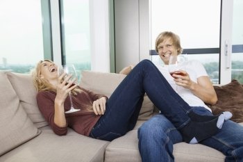 Cheerful relaxed couple with wine glasses in living room at home