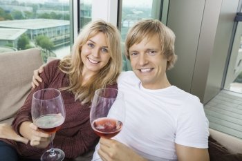 Portrait of happy couple with wine glasses in living room at home