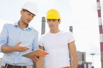 Male construction workers discussing over digital tablet at industry