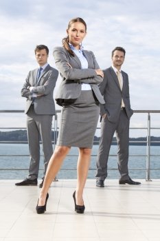Full length portrait of confident businesswoman standing with coworkers on terrace against sky