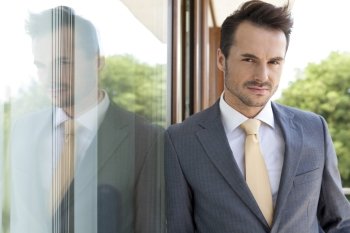 Portrait of confident businessman leaning on glass door