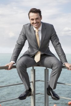 Full-length portrait of happy businessman sitting on terrace railings