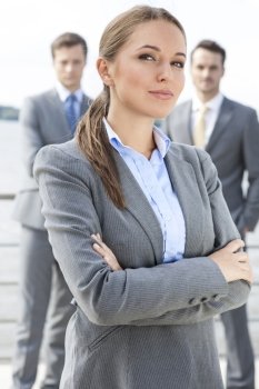 Portrait of confident businesswoman standing arms crossed with coworkers in background on terrace
