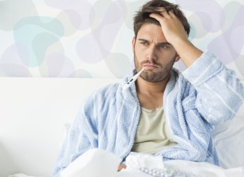 Sick man with thermometer in mouth sitting on bed at home