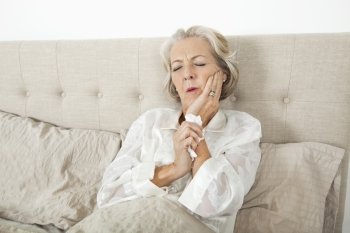 Senior woman suffering from toothache resting in bed