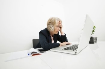 Stressed senior businesswoman using laptop at desk in office