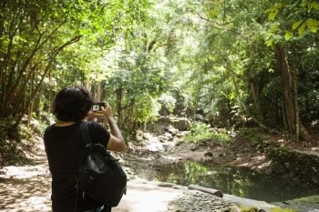 Rear view of young male hiker photographing in forest; Koh Pha Ngan; Thailand