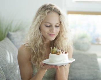 Beautiful young woman looking at tempting cake in house