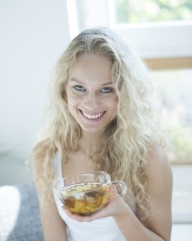 Portrait of happy young woman holding herbal tea cup in house