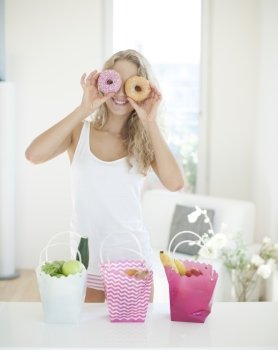 Happy woman holding donuts in front of eyes at kitchen counter