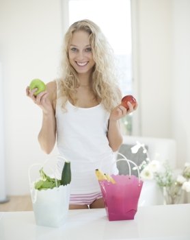 Portrait of young woman holding apples at kitchen counter