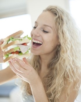 Happy woman eating large sandwich in house
