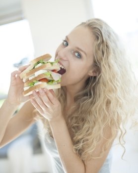 Portrait of impatient woman eating large sandwich in house