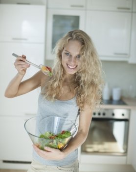 Portrait of happy woman mixing salad in kitchen