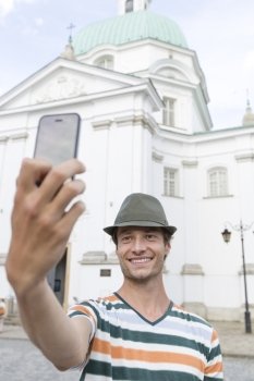 Young man taking self portrait outside St. Casimir Church; Warsaw; Poland