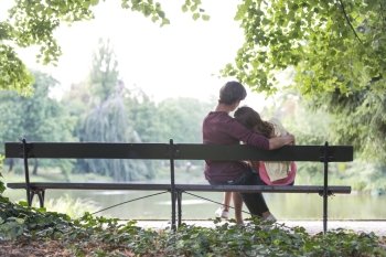 Rear view of romantic young couple sitting on bench at lakeside