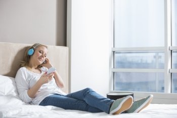 Full length of relaxed woman listening music in bedroom