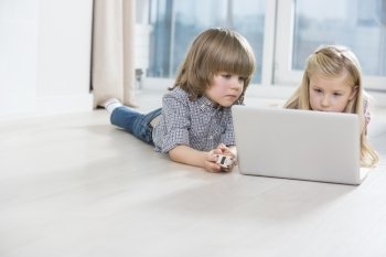 Brother and sister using laptop on floor at home