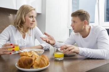 Mid adult couple talking while having breakfast at home