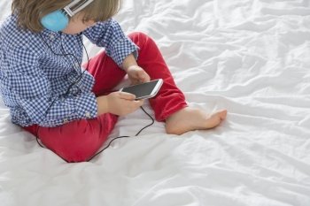 High angle view of boy listening to music through smart phone in bedroom