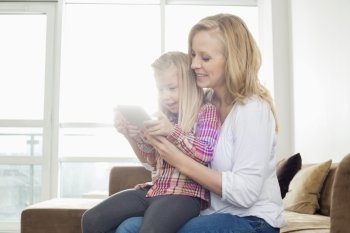 Happy woman with daughter using digital tablet in living room