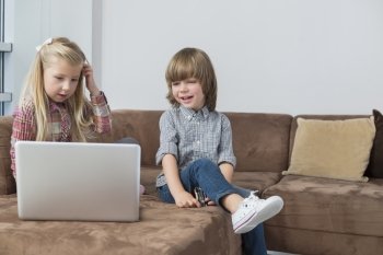 Happy boy with sister using laptop on sofa