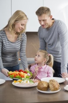 Happy parents with daughter having meal in kitchen