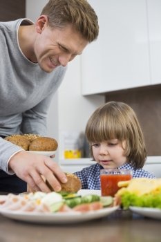 Happy father serving meal to son at table in kitchen