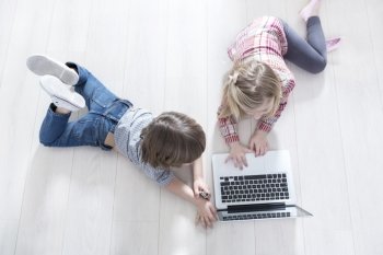 High angle view of brother and sister using laptop on floor at home